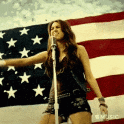 a woman is standing in front of an american flag singing into a microphone .