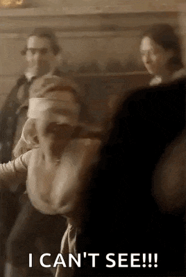 a woman with blindfolds on her eyes is walking in a room with other people .