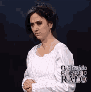 a woman in a white dress is standing on a stage with her hands folded .
