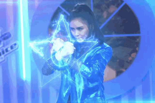 a woman in a blue jacket is standing in front of a wall that says voice