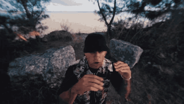 a man wearing a black hat and a floral shirt stands in a field