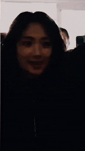 a woman with long hair is standing in a dark room with a man behind her .
