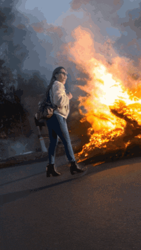 a woman walking in front of a fire