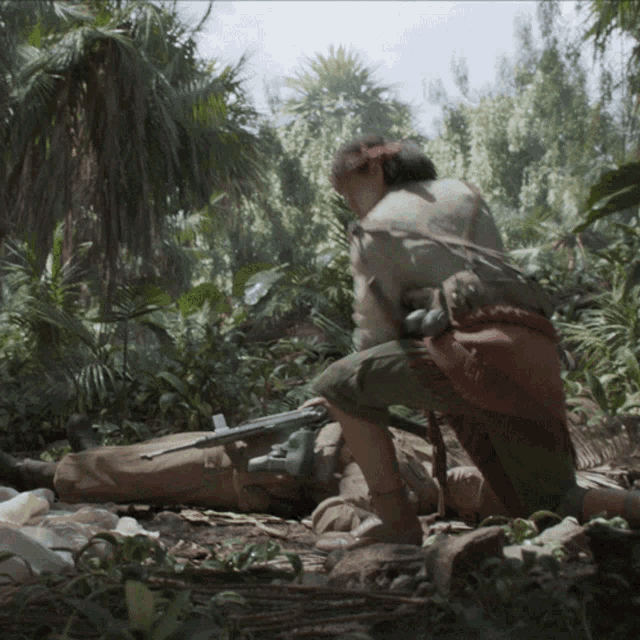 a man kneeling down in a jungle with a gun