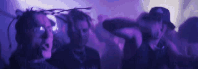 a group of people are dancing in a dark room in purple light .