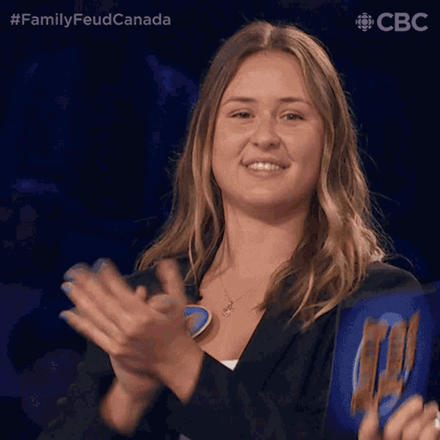 a woman applauds in front of a screen that says familyfeud canada