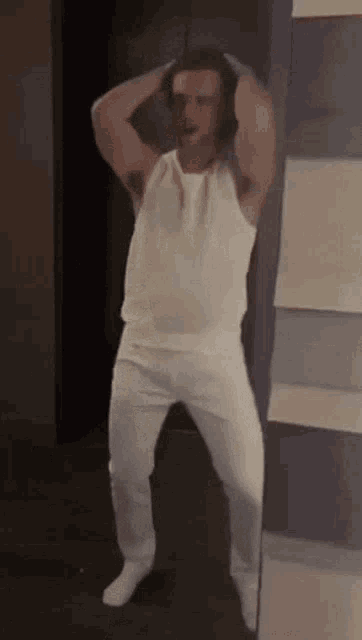 a man in a white tank top and white pants is standing in a hallway .