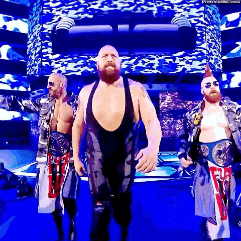 a group of wrestlers are walking on a stage holding their belts .