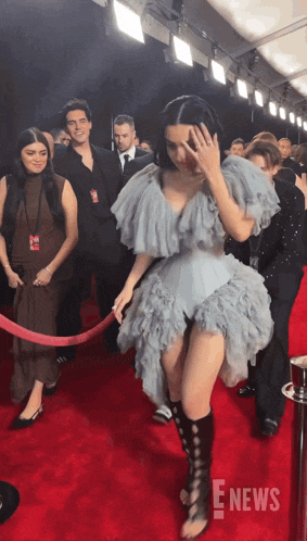 a woman in a ruffled dress walks on a red carpet with the e news logo in the corner