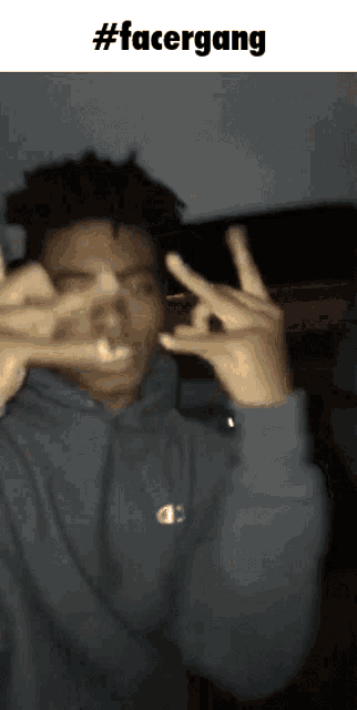 a man in a grey hoodie is making a face with his hands
