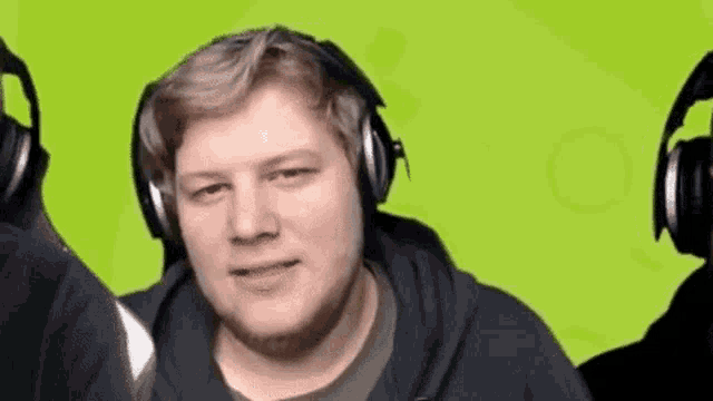 a man wearing headphones is making a funny face while standing in front of a green background .
