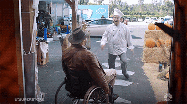 a man in a wheelchair is standing next to a man in a chef 's hat