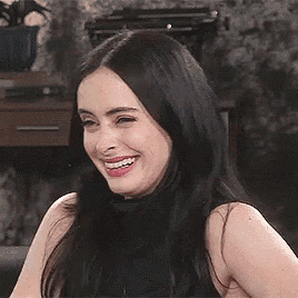 a woman with long black hair is laughing while wearing a black tank top .