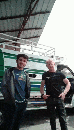 a man wearing a shirt that says " too 1312 " stands next to a man wearing a black shirt