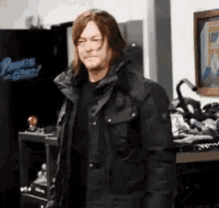 a man in a black jacket is standing in a room in front of a motorcycle .