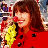 a woman in a red coat is smiling while holding a strawberry in her mouth .