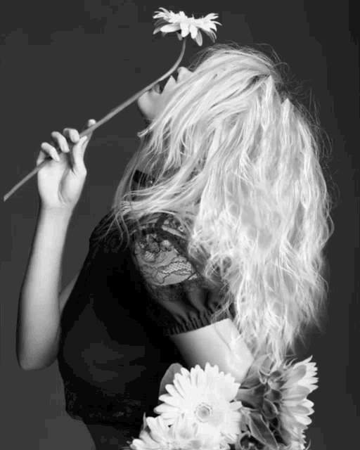 a woman with blonde hair is holding a flower to her nose