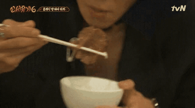 a person is eating something from a bowl with chopsticks and a tvn logo in the corner
