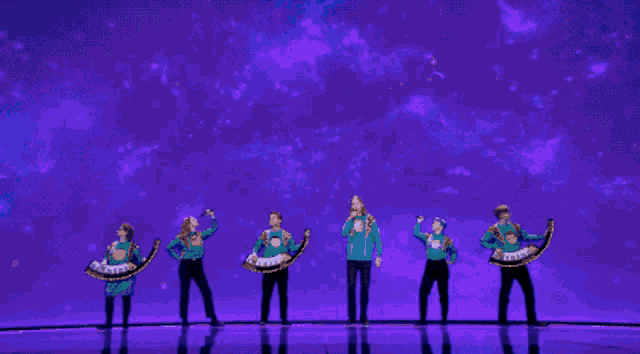 a group of people are performing on a stage and one of them is singing into a microphone