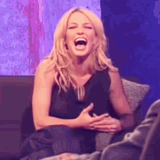 a woman is laughing while sitting on a couch with her hands on her chest .