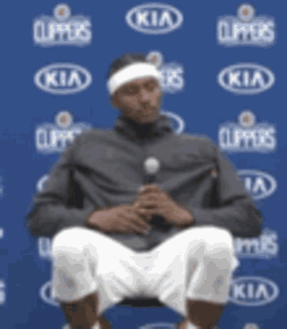 a man wearing a headband is sitting in front of a kia sign