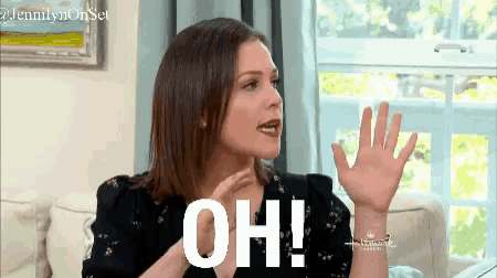a woman is sitting on a couch with her hand up and says oh !