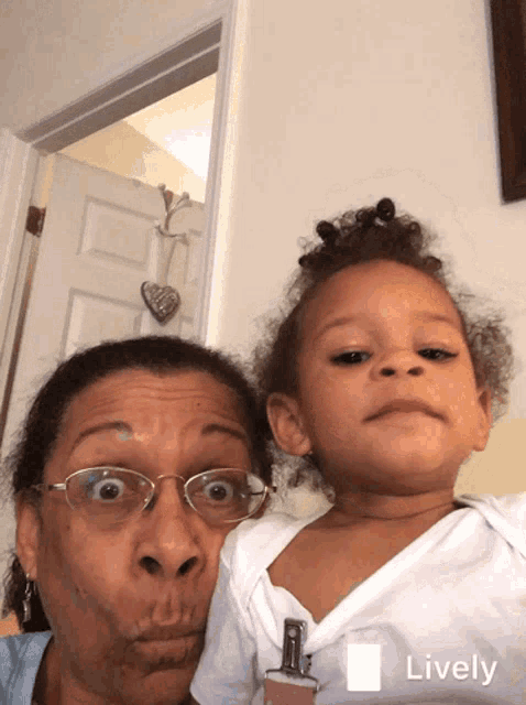 a woman with glasses is holding a little girl who is wearing a white shirt with a lanyard around her neck
