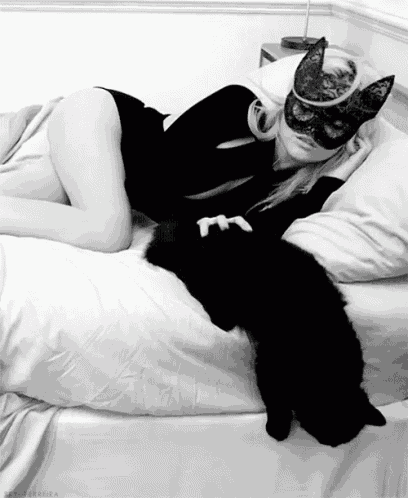 a woman wearing a mask is laying on a bed with her cat