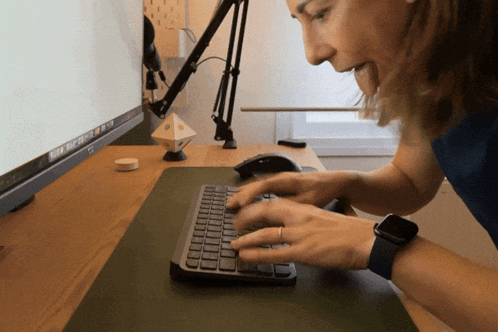 a woman is typing on a keyboard in front of a monitor that says mac os x