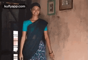 a woman in a blue shirt and black saree is standing in a room .