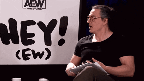 a man sitting in front of a sign that says hey ew