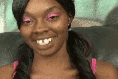 a woman with pigtails and pink eye shadow is smiling and sitting on a couch .