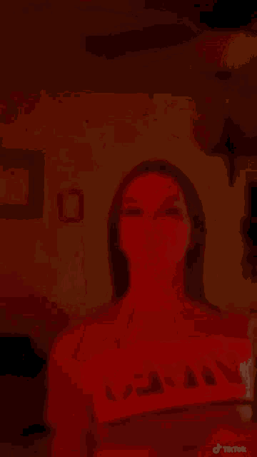 a woman is holding a cup of popcorn in a dark room with red lights .