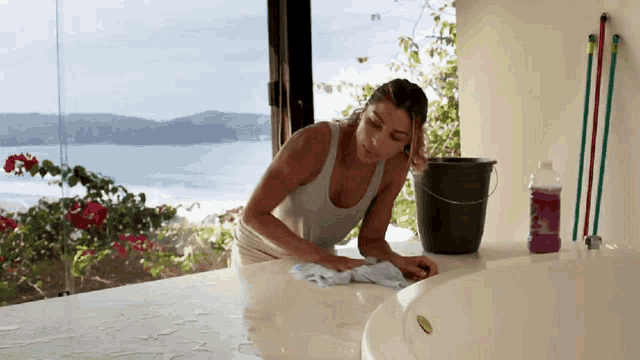 a woman is cleaning a bathtub with a bucket and a bottle of cleaner
