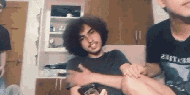 a man with curly hair is sitting on a couch with another man .