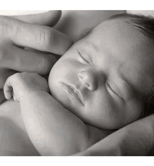 a black and white photo of a baby sleeping in a person 's arms
