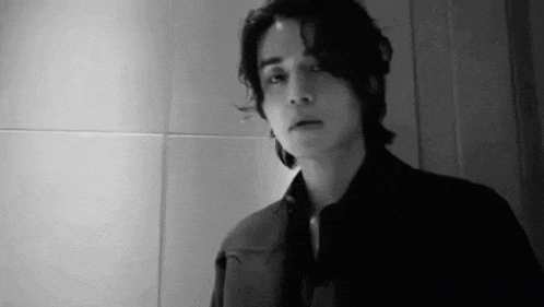 a black and white photo of a man in a suit standing in front of a wall .