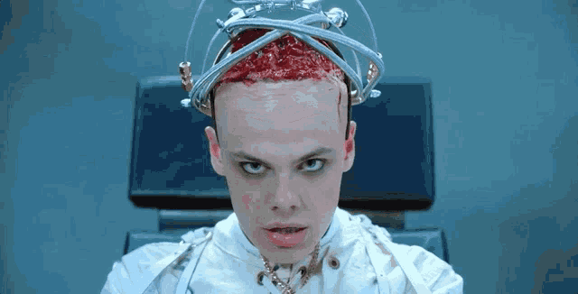 a man with a crown on his head is sitting in a chair with blood on his head .