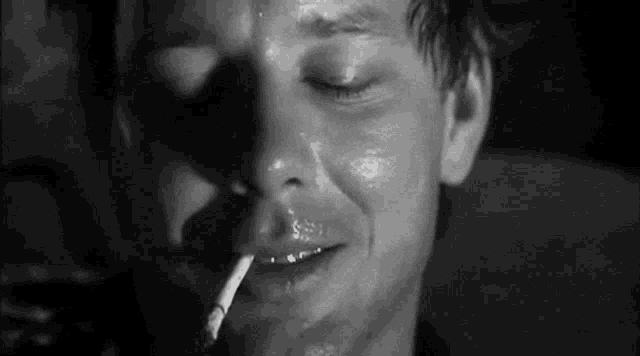 a man is smoking a cigarette in a black and white photo with his eyes closed .