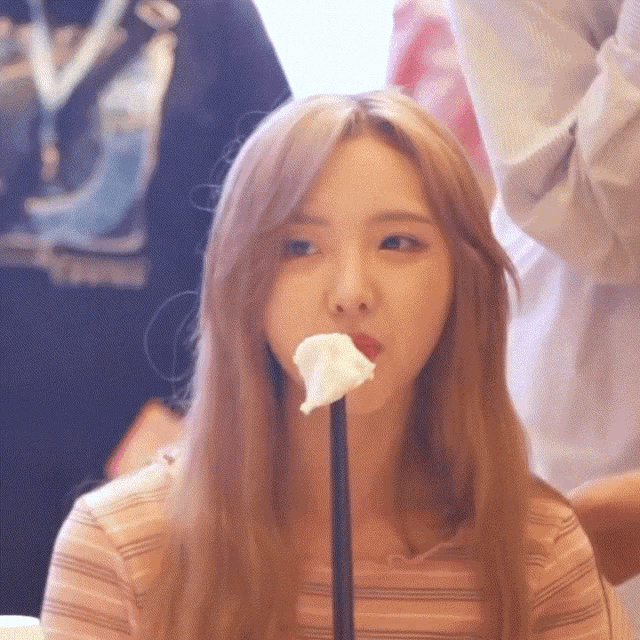 a woman with long blonde hair is eating a piece of marshmallow on a stick
