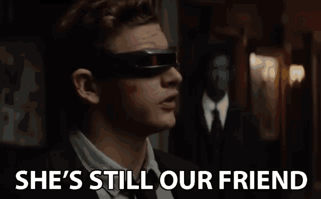 a man wearing sunglasses says she 's still our friend in front of a man in a suit