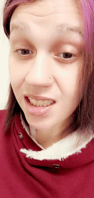 a woman with purple hair is wearing a red sweatshirt
