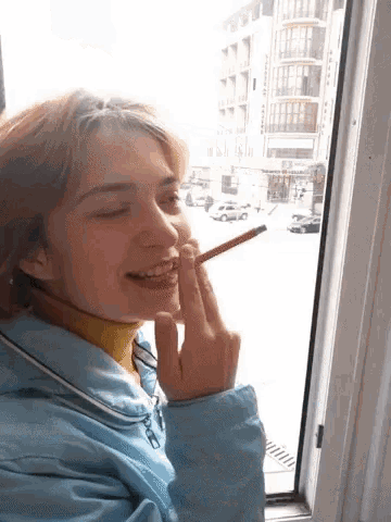 a woman with a pencil in her mouth looks out of a window