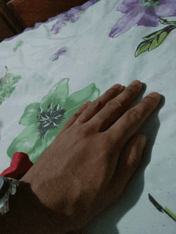 a person 's hand rests on a table cloth with purple and green flowers