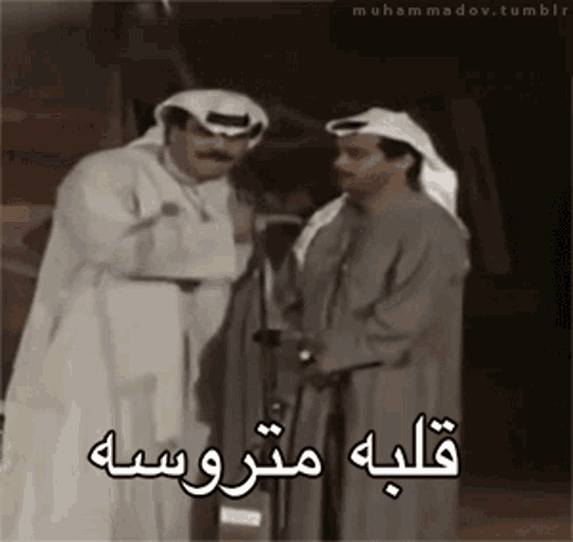 two men standing next to each other with arabic writing on the bottom right