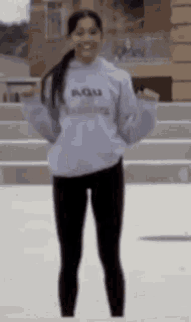a woman wearing a grey hoodie and black leggings is standing in front of a building .