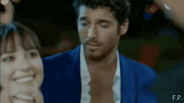 a man in a blue jacket is smoking a cigarette next to a woman with f.p. written on the bottom