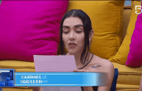 a woman is sitting on a couch reading a piece of paper with the name karimelle queeenny on it