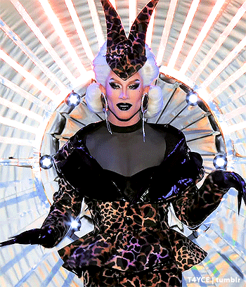 a drag queen wearing a leopard print dress and a horned hat is standing in front of a circle of lights