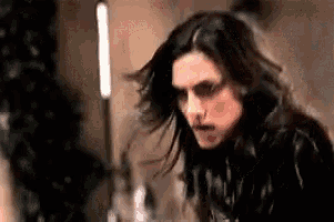 a man with long hair and glasses is standing in front of a candle .